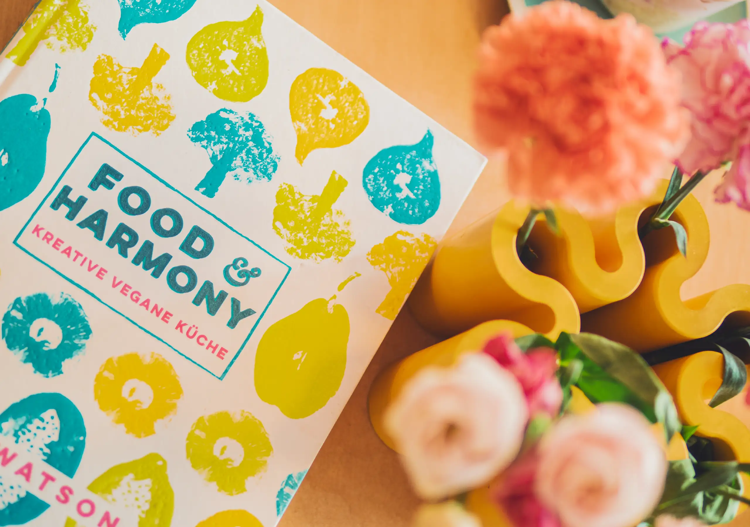 Nahaufnahme des Buches „Food & Harmony“ neben gelben Vasen und Blumen als Inspirations-Stillleben.