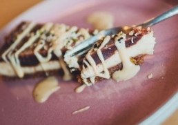 Detailaufnahme eines veganen Cheesecake-Stücks auf rosa Teller mit hellem Mandelmus.