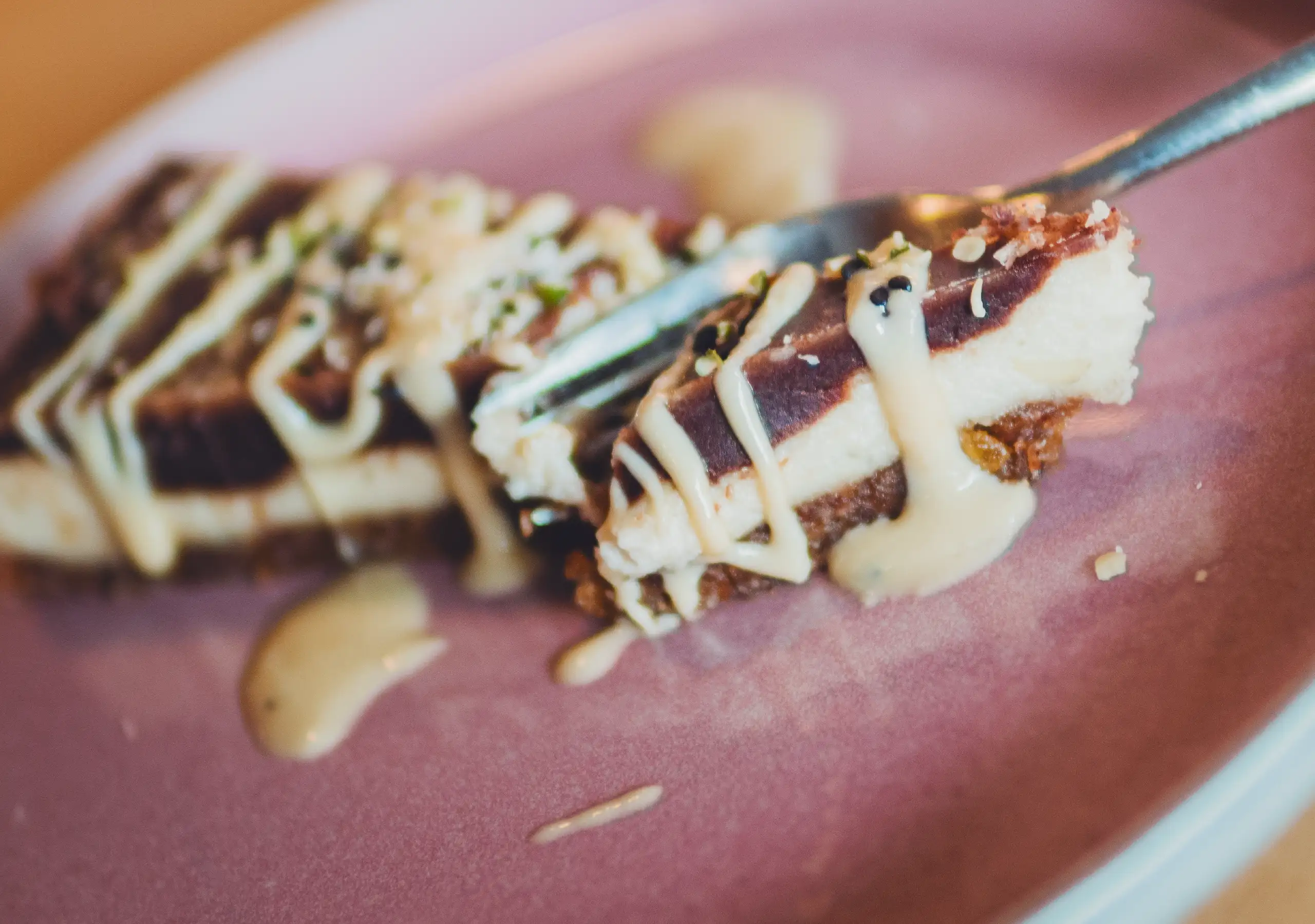 Detailaufnahme eines veganen Cheesecake-Stücks auf rosa Teller mit hellem Mandelmus.