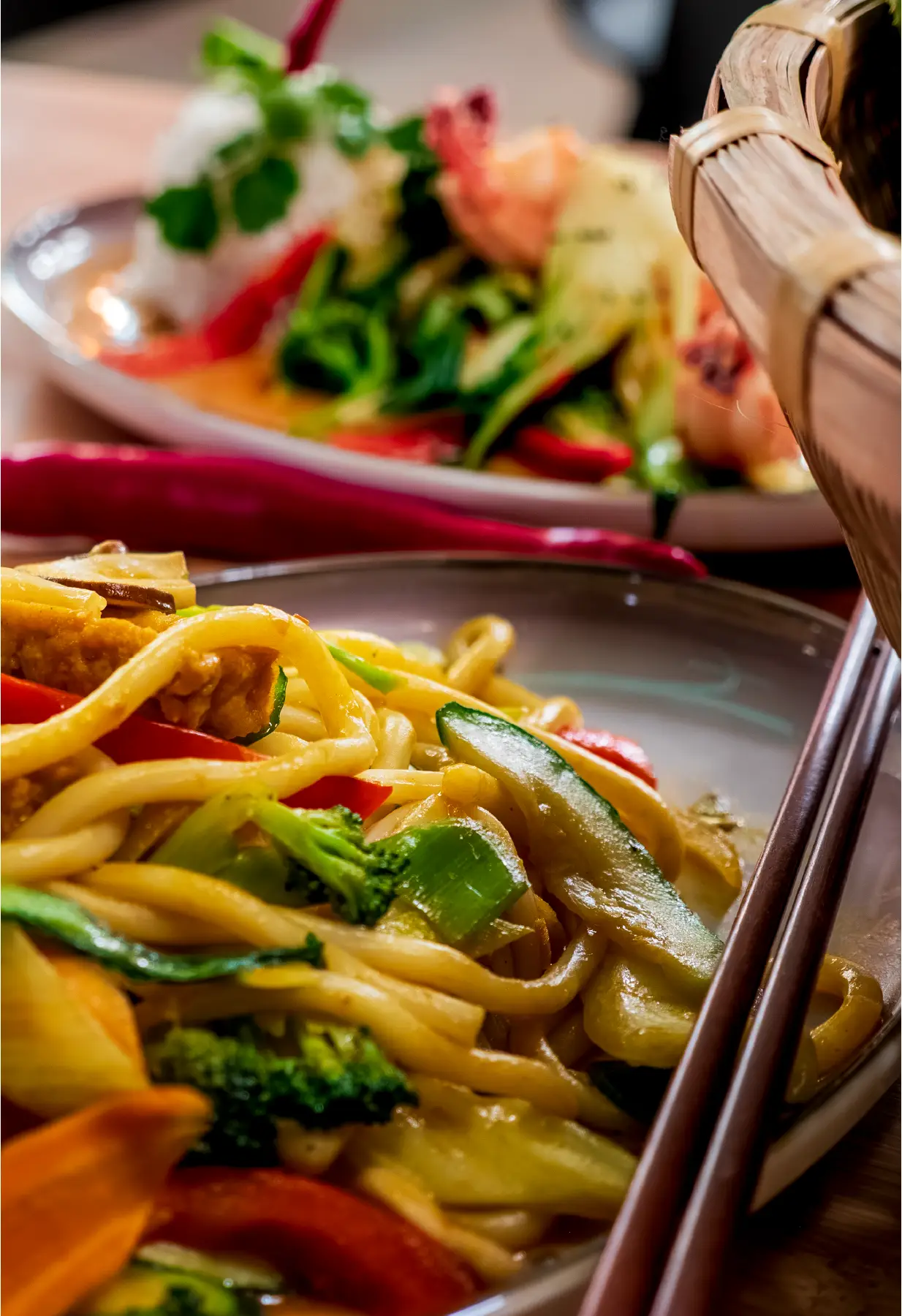 Detailaufnahme von Wok-Nudeln mit Zucchini, Brokkoli und Paprika, Essstäbchen im Vordergrund.
