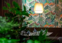 Restaurantinterieur mit farbiger, illustrativer Tapete und warmem Licht, Pflanzen im Vordergrund.