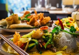 Teller mit Reisdom, Garnelen und Gemüse in gelber Sauce, Frühlingsrollen im Hintergrund.