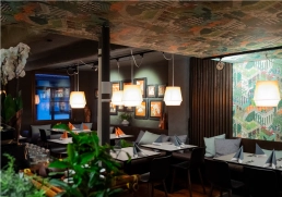 Restaurantinterieur mit farbiger, illustrativer Tapete und warmem Licht, Pflanzen im Vordergrund.