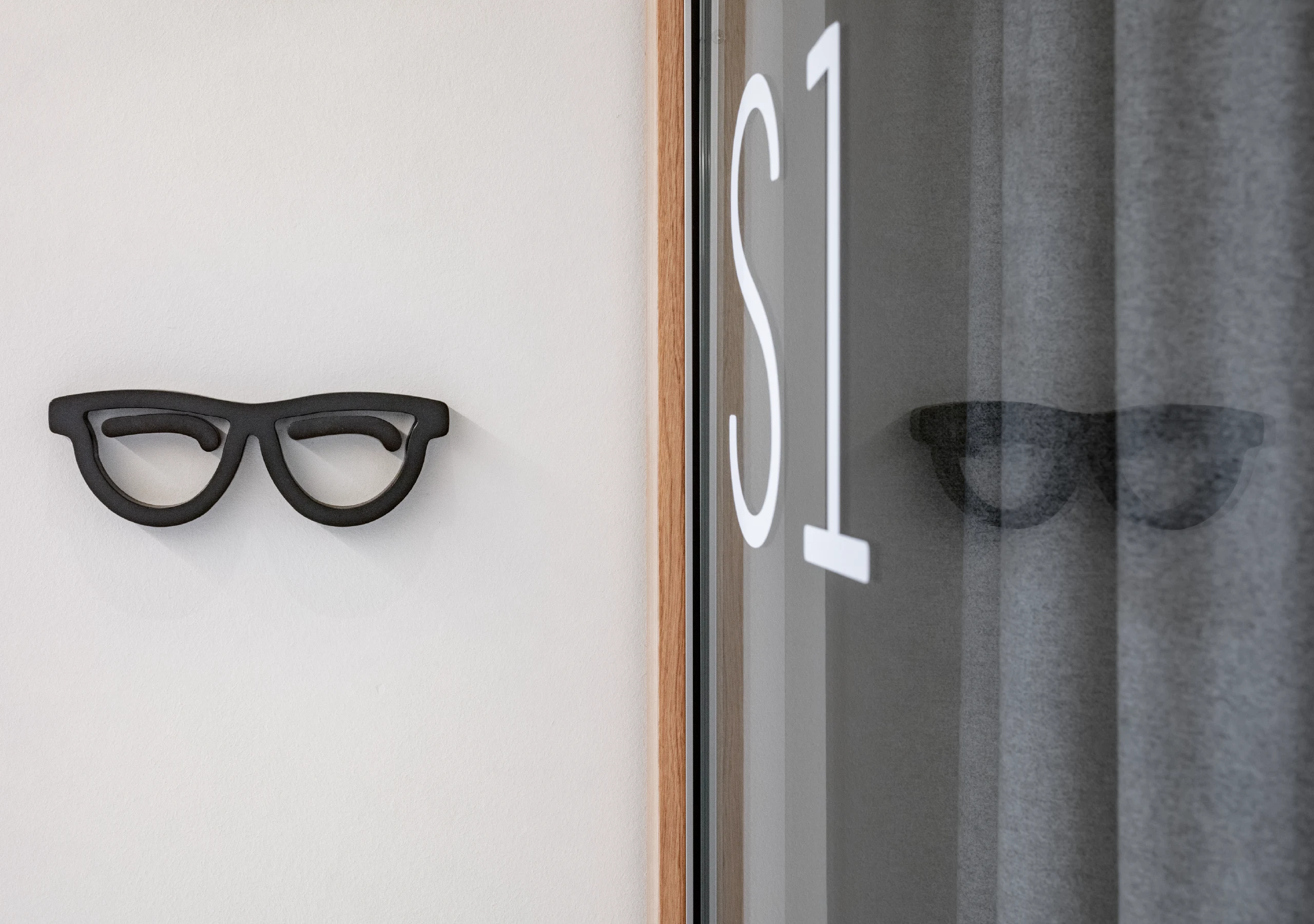 Schwarzes Brillen-Piktogramm an Wand neben Glastür S1.