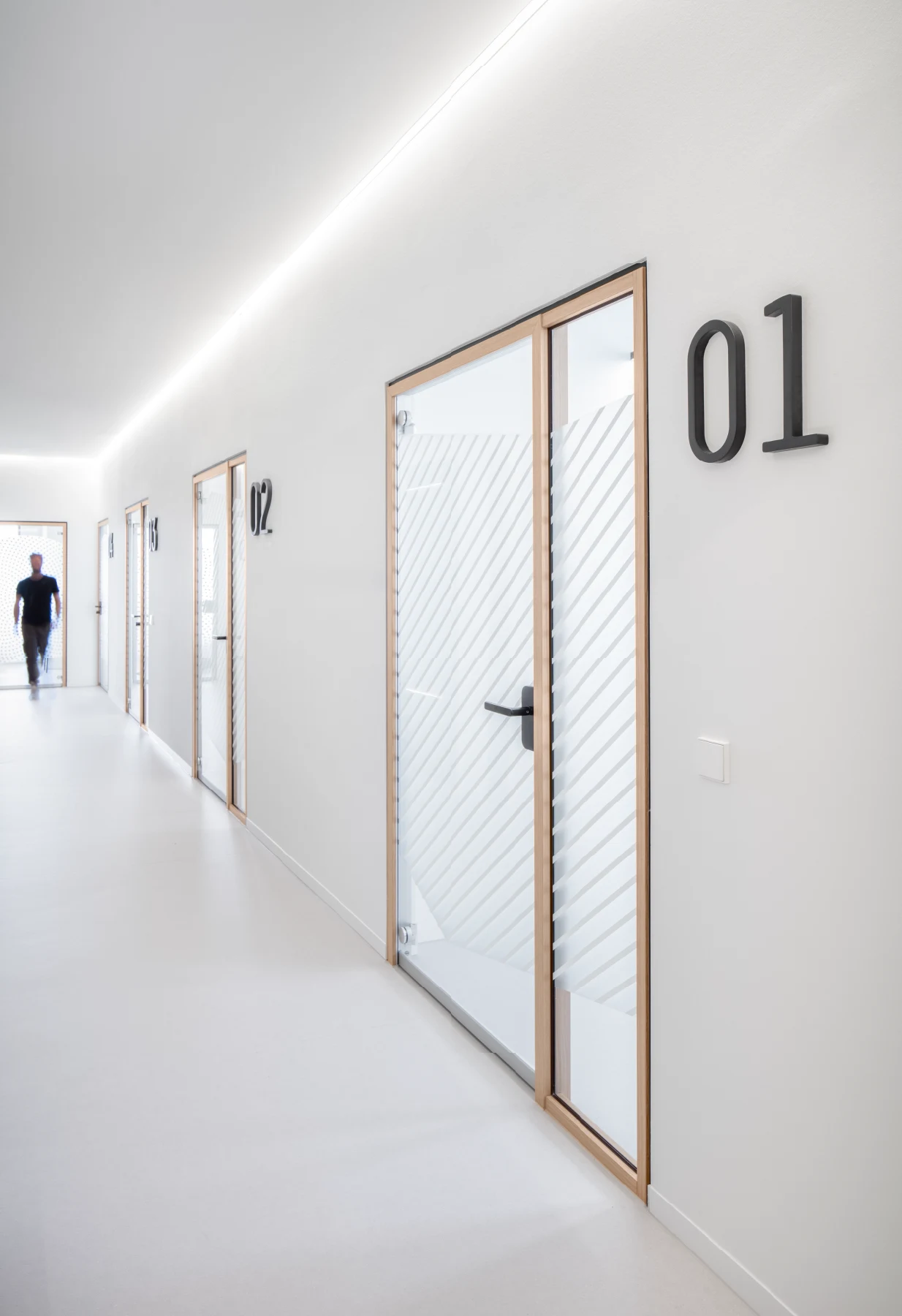 Langer, heller Korridor mit Türen 01–03, LED-Lichtvoute, Glas mit Diagonalen.