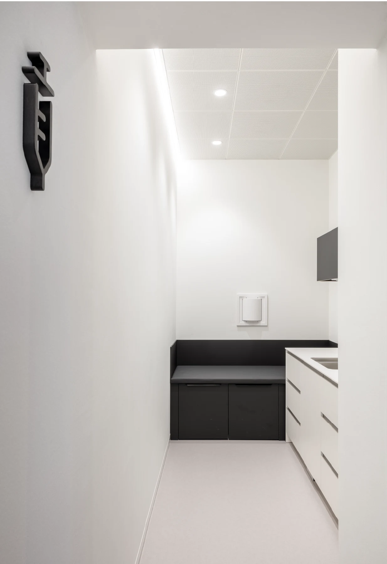 Schlanker Behandlungsraum mit Spritzen-Piktogramm, weißen Fronten und LED.